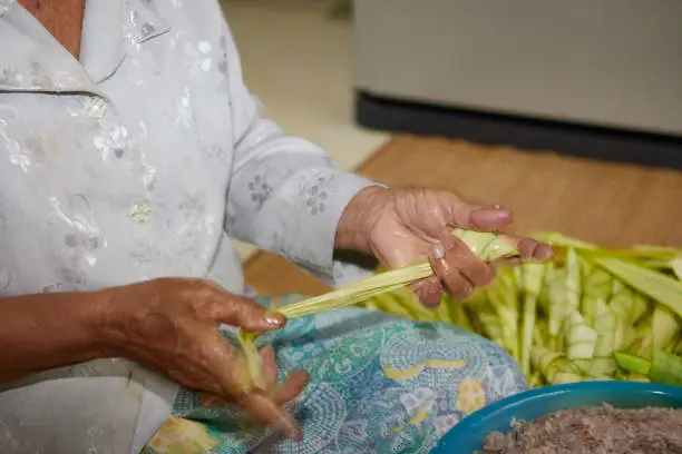 Photo of Hands of senior woman wrapping the sticky rice with palm leaf or Ketupat Palas