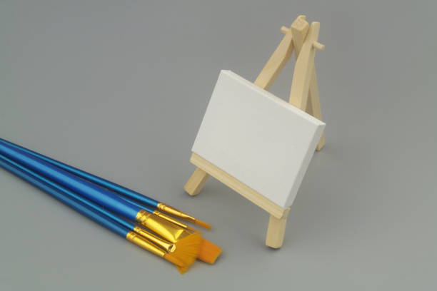 istock Many paintbrushes and easel with blank canvas on gray background. 1437425403