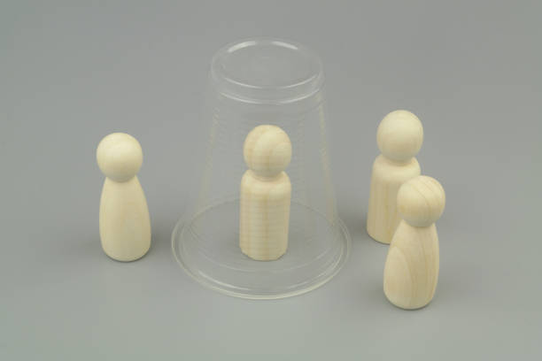 istock Wooden people figures on gray background. One figure under plastic cup. 1437428442