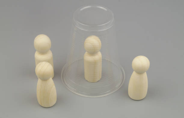 istock Wooden people figures on gray background. One figure under plastic cup. 1437428458