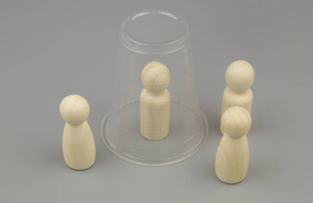 istock Wooden people figures on gray background. One figure under plastic cup. 1437428473
