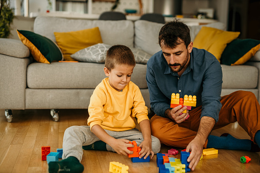 Shot of a young boy and his father playing with cubes on the floor, bonding time between father an son at home.
