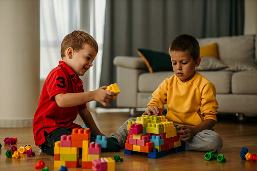 Shot of two young boys playing with building blocks in a room. Boys sitting on the floor and playing with toys alone.