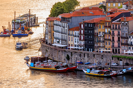 Porto, Portugal - May 30, 2018: Facades of traditional colorful Portuguese houses in Ribeira and rabelo boats docked on Douro at sunset golden hour