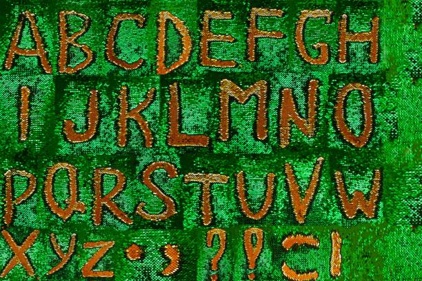 istock Alphabet sequins. Golden sequins letters on green sparkling sequins background.Shining letters on a shiny background. Festive Christmas alphabet .Symbols and signs 1437435059