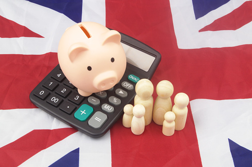 Cost of living and saving money in United Kingdom. Family people figures with calculator and piggy bank on British flag.