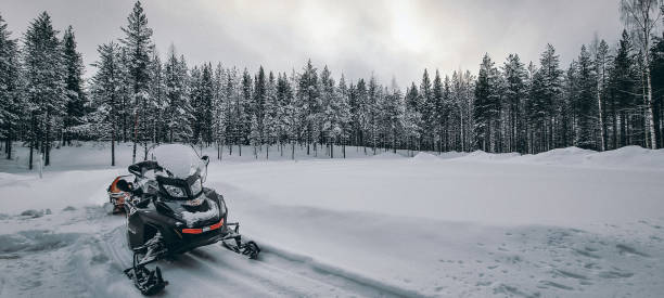 una moto de nieve aparcada en la nieve y bosque de pinos al fondo - motoesquí fotografías e imágenes de stock