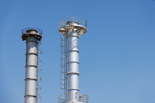 High section of two smokeless industrial metallic chimneys against the blue sky, fuels supply cut off due to price escalation, energy crisis