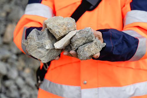 Male road worker standing on the road and holding stones from rock slide in the mountains