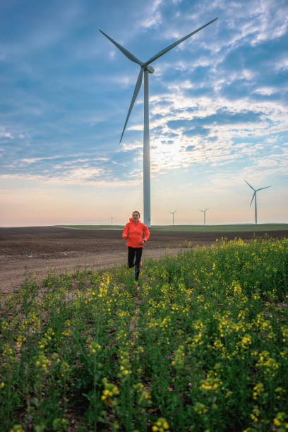 istock Young woman running through plants on wind farm under the cloudy sky 1437445295