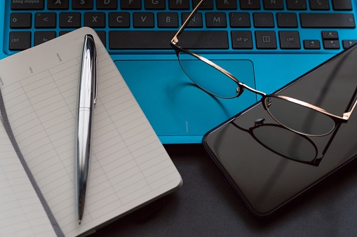 A high angle shot of a pair of glasses with a pen and a notebook on a laptop keyboard