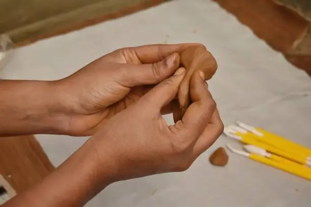 A Closeup view of a Women Hands making Clay Model of Ganesh for Ganesh Chaturthi with Clay tools in Background. Clay Modelling art is good Hobby