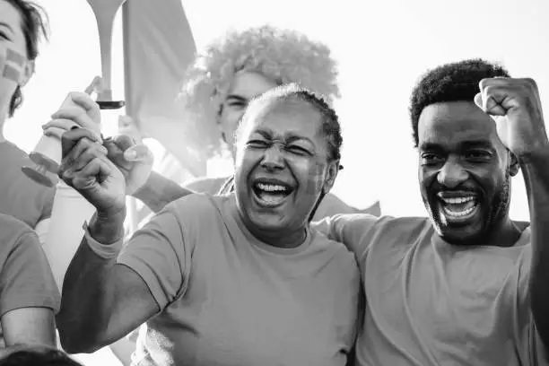 African sport soccer fans shouting and celebrating team winning championship game at stadium - Football supporter having fun in crowd - Black and white edition