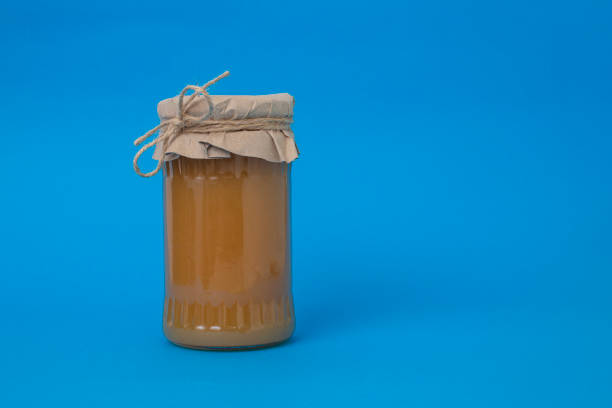 Apple marmelade in a glass jar covered with paper, on blue background.