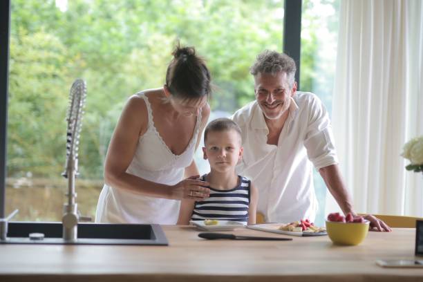 parents and their son standing against the kitchen counter with food on it under the sunlight - two parent family indoors home interior domestic kitchen imagens e fotografias de stock