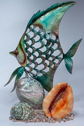 A vertical shot of a fish figurine with different seashells under it on a white surface and background