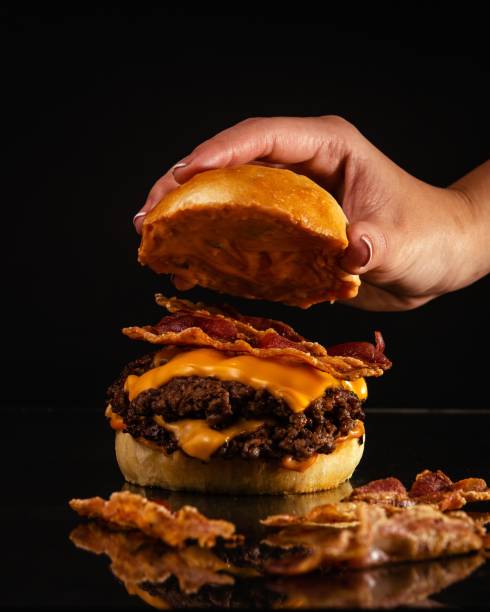 istock Person preparing a delicious burger with beef, yellow cheese, and bacon 1437457777