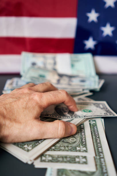 Close-up of a man's hand holding an amount of dollars. A Close-up of a man's hand holding an amount of dollars, with a United States flag in the background. greedy corporation stock pictures, royalty-free photos & images