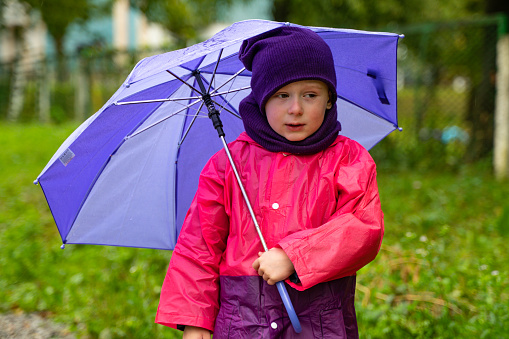 Child playing in autumn rain. Kid with umbrella. Outdoor fun for kids by any weather. Rain waterproof wear, boots and jacket for children.