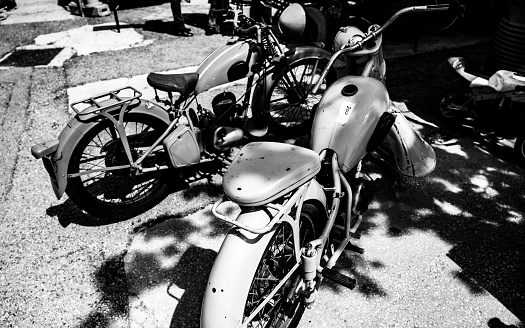 A grayscale shot of retro motorbikes parked close to the shadow cast from the trees
