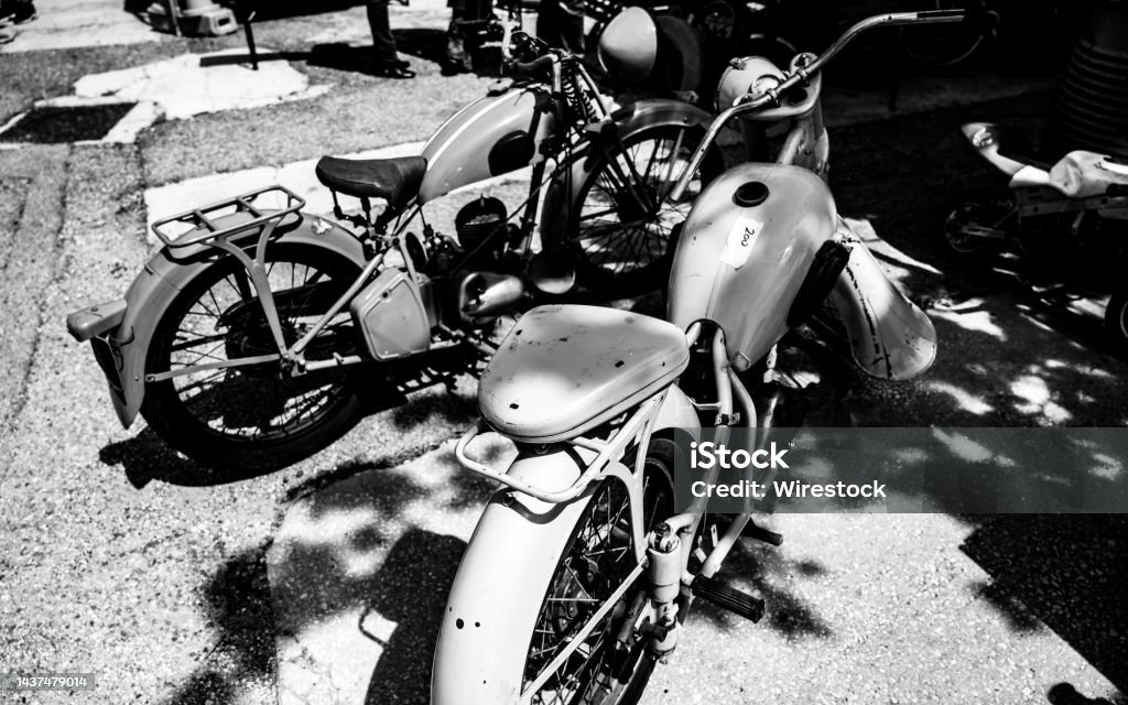 Grayscale shot of retro motorbikes parked close to the shadow cast from the trees A grayscale shot of retro motorbikes parked close to the shadow cast from the trees Antique Stock Photo