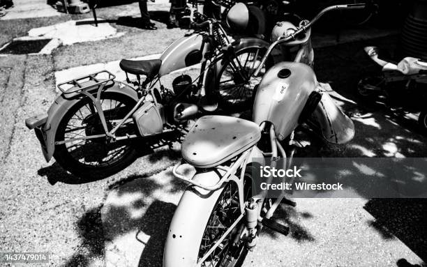 Grayscale Shot Of Retro Motorbikes Parked Close To The Shadow Cast From The Trees Stock Photo - Download Image Now