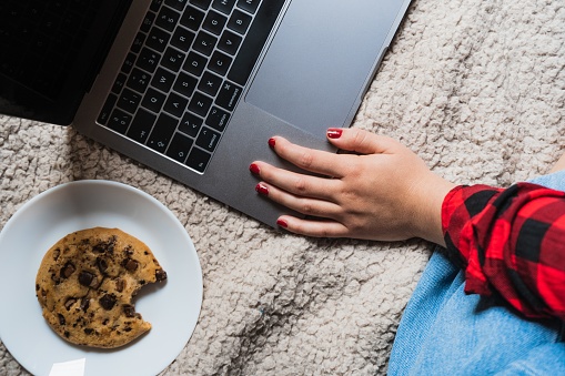 A horizontal shot of a female sitting on a blanket with her laptop and a cookie