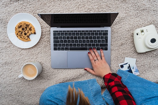 A horizontal shot of a female sitting on a blanket with her laptop and coffee