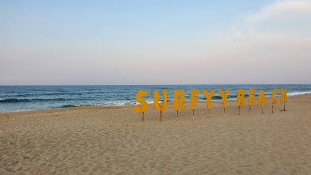 bellissimo scatto grandi lettere gialle in piedi nella sabbia che scandiscono [surfy beach] sullo sfondo del mare - surfy foto e immagini stock
