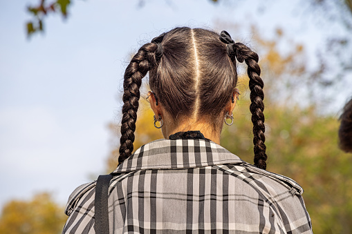 Venice, Italy - October 6th 2022: Young woman with significant pigtails seen from behind in a public park in the center of the old and famous Italian city Venice