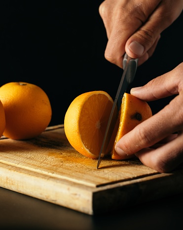 A vertical shot of a person cutting oranges on a wooden board under the lights