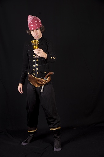 A vertical shot of a male in a pirate costume drinking from a golden glass