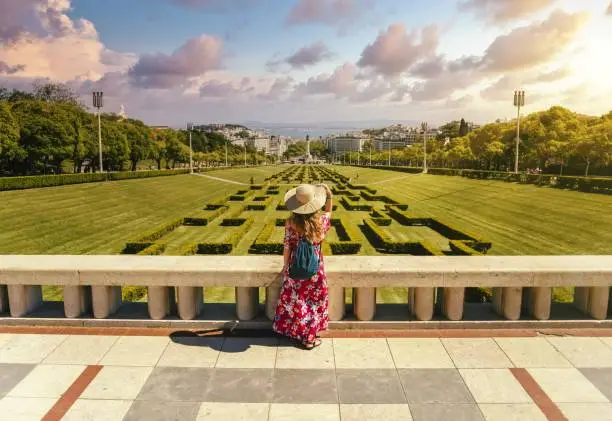 Photo of Young female tourist in a red floral dress in The Eduardo VII Park under the sunlight in Portugal