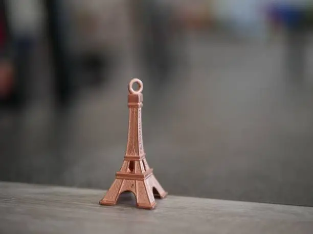 Photo of Closeup shot of a small Eiffel Tower keychain on a suface in a blurred background