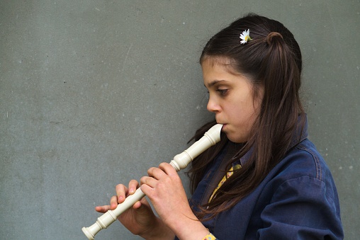 A young girl playing a recorder isolated on a gray background