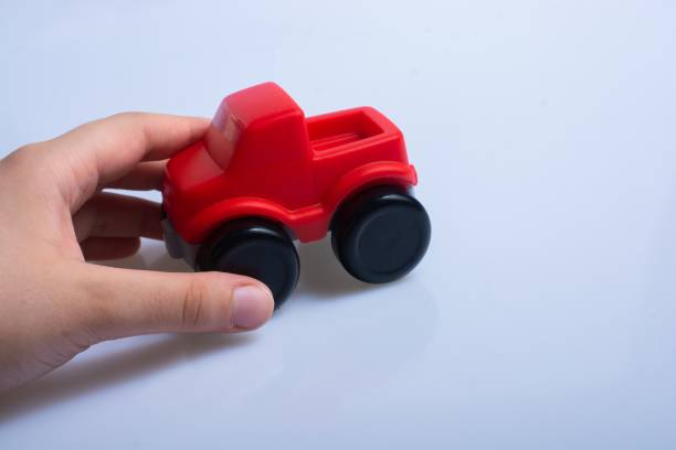 istock Person's hand holding a red plastic toy car on a white surface 1437485398