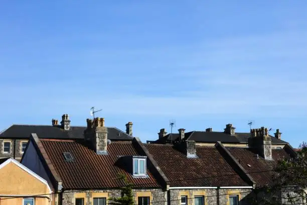 The victorian-style rooftops with chimney of houses in a residential area with blue sky in Bristol, UK