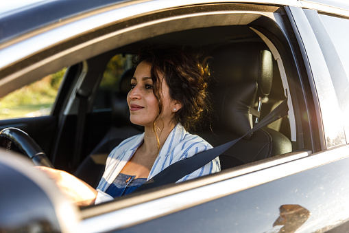 Portrait of happy mid adult woman sitting in her car, looking at the road while driving.