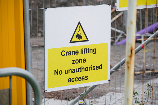 Crane lifting safety sign on construction site fence UK