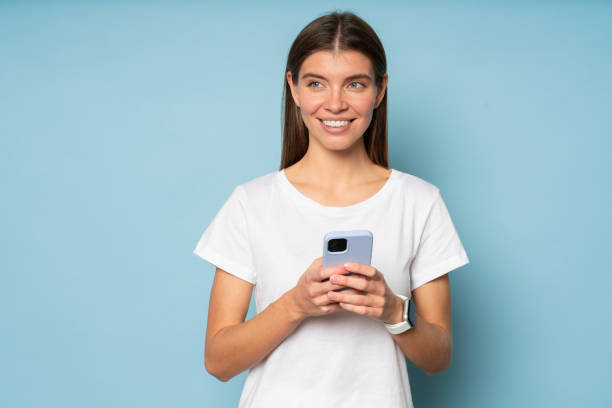 istock Woman using phone on blue background looking aside thinking over her respond in online chat 1437494432