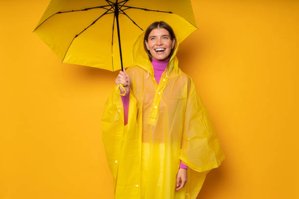 femme en imperméable imperméable jaune avec parapluie vérifiant la pluie debout sous le parasol - rain women umbrella parasol photos et images de collection