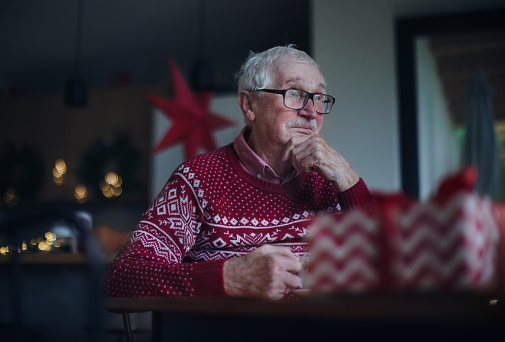 Unhappy senior man sitting alone and waiting for family during Christmas Eve.Concept of solitude senior and mental health.