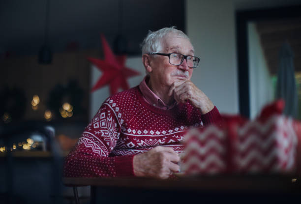 Unhappy senior man sitting alone and waiting for family during Christmas Eve.Concept of solitude senior and mental health. stock photo