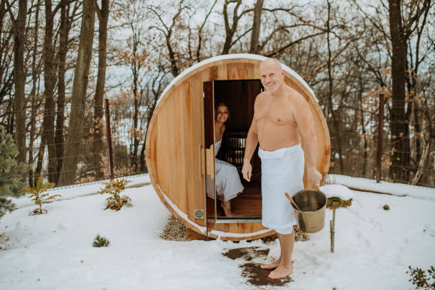 пожилая женщина в полотенце с мужем входит в сауну на открытом воздухе холодным зимним днем. - sauna health spa healthy lifestyle wellbeing стоковые фото и изображения