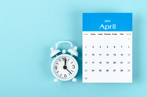 April 2023 Monthly calendar for 2023 year with vintage alarm clock on blue background.