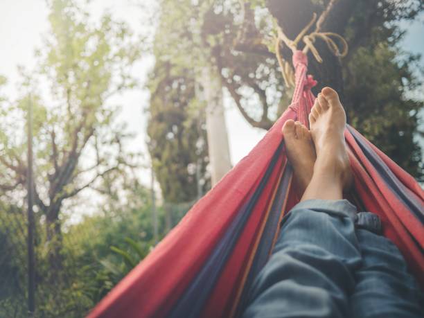 istock Barefoot man with blue jeans lying on a red hammock and some trees in the background 1437504932