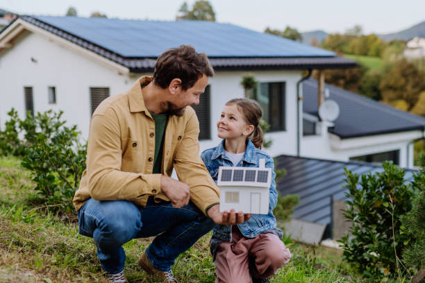Little girl with her dad holding paper model of house with solar panels, explaining how it works.Alternative energy, saving resources and sustainable lifestyle concept. stock photo