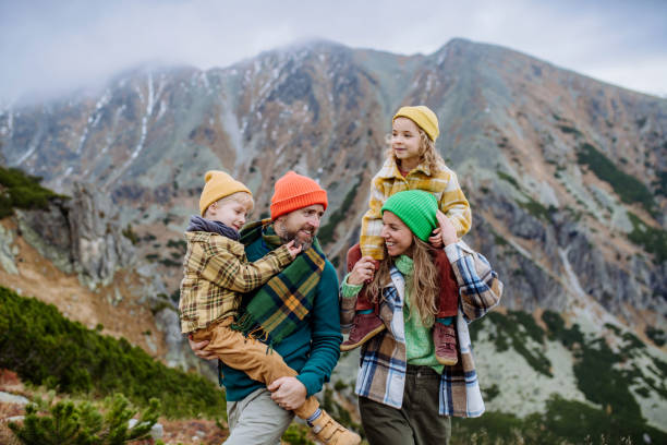 Happy parents with their little kids on piggyback at autumn hike, in the middle of mountains. Concept of healthy lifestyle. Happy parents with their little kids on piggyback at an autumn hike, in the middle of mountains. Concept of healthy lifestyle. high tatras stock pictures, royalty-free photos & images