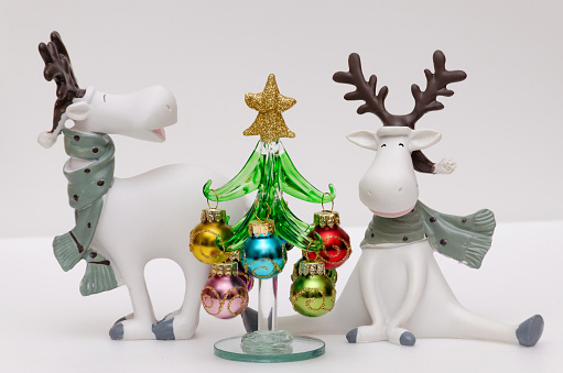 Close-up photo of funny deer figurines and a Christmas tree with bright balls. Winter composition. New Year card