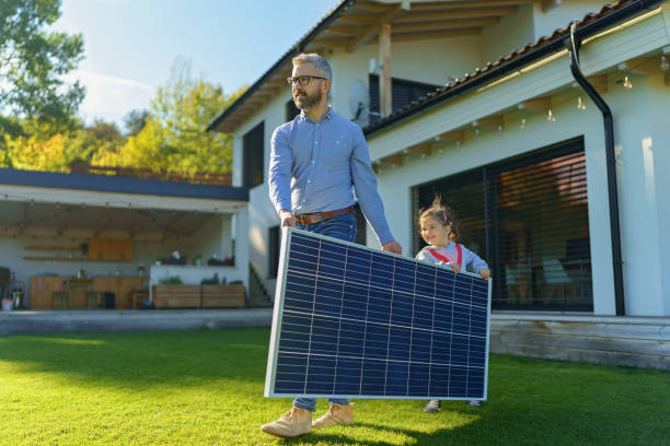 Father with his little daughter carring solar panel at their backyard. Alternative energy, saving resources and sustainable lifestyle concept. stock photo